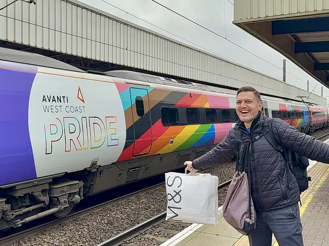 Andy in front of Avanti West Coast train featuring "Manchester Pride" livery